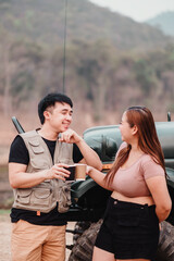 Casual and lively conversation unfolds between a young couple, with coffee in hand, beside their parked off-road car.