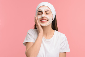 Young woman with headband washing her face on pink background