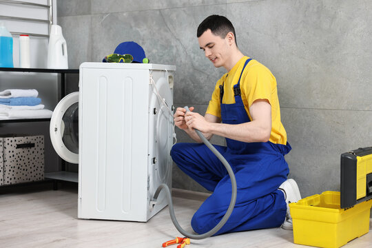 Young plumber examining drain hose of washing machine in bathroom