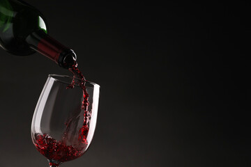 Pouring tasty red wine from bottle into glass on dark background, closeup. Space for text
