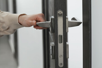 Woman opening wooden door indoors, closeup of hand on handle