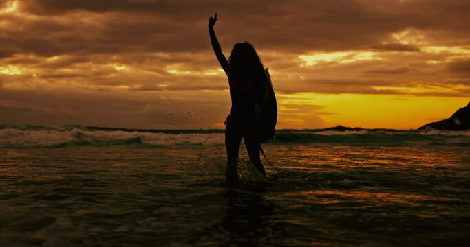 Sunset, silhouette and woman with a surfboard, seaside and water with adventure and vacation. Person, girl and surfer with ocean or beach with shaka sign and summer with nature or travel with journey