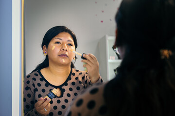 latina woman putting make-up foundation on her face - beauty concept