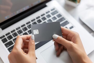 Close up of a woman's hands holding a gray credit card in front of a laptop computer - obrazy, fototapety, plakaty