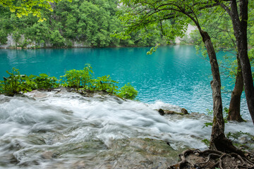 turquoise pond surrounded by foliage with water smoothed in motion flowing over rock in Croatia