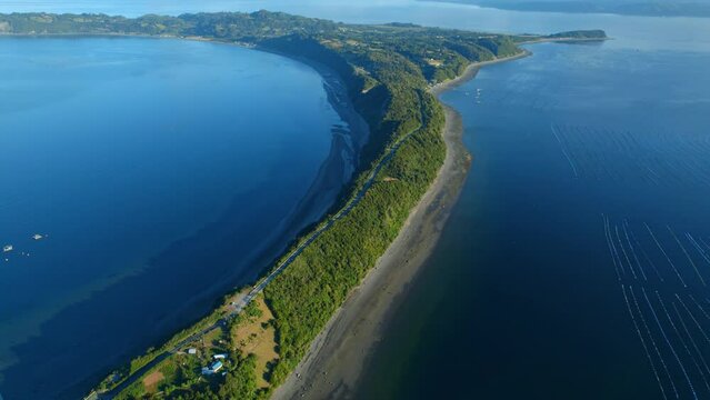 Drone shot over a sharp bend, narrow channel linking Lemuy Island to Detif, fishing farms on the sides, Chiloe, natural environment.