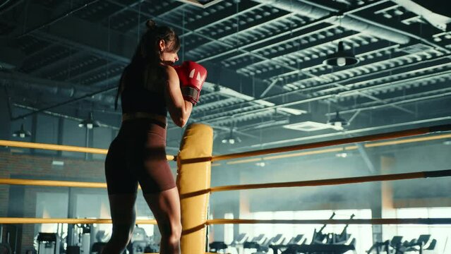 A determined female boxer trains her punching technique in a contemporary, sunlit boxing gym, exhibiting agility and strength with her powerful strikes. Camera 8K RAW. 