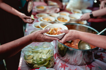 The hand of the wanderer extends to receive food from donations. With volunteers scooping food: the idea of helping with hunger