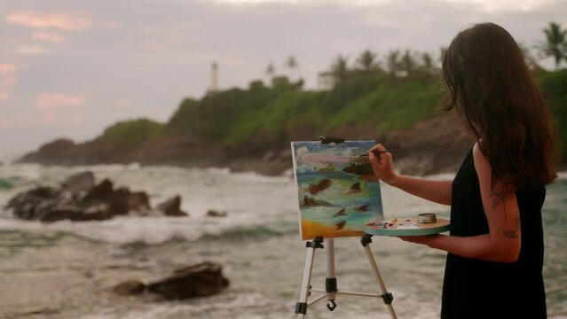 Artist paints seascape on canvas at stormy beach, dusk light. Waves crash, female painter captures ocean mood. Creative process by sea, art inspiration, tranquil coastal scene at twilight. Slowmo
