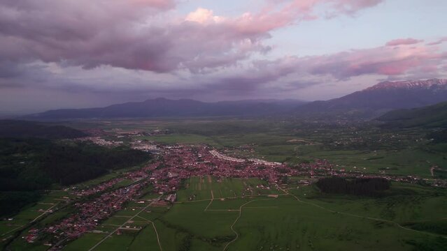 Zarnesti city at sunset with pink clouds and surrounding landscape, aerial view