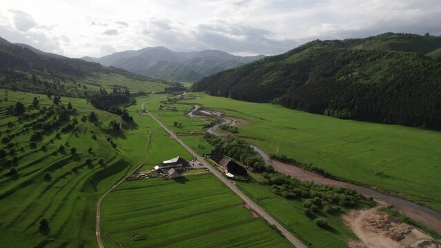 Lush green valley near Zarnesti with farms and winding road, cloudy sky, aerial view