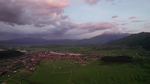 Sunset hues over Zarnesti city with rolling hills and lush fields, aerial view