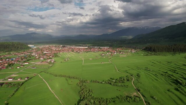 Verdant fields near Zarnesti with picturesque mountains under a dynamic sky, aerial view