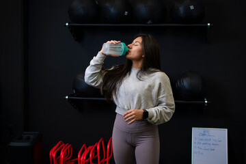 female athlete taking protein from her shaker before her gym workout