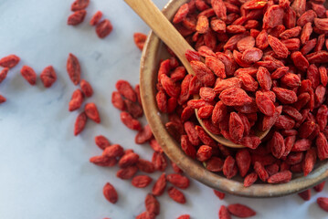 Dried  goji berries in ceramic plate with wooden spoon.