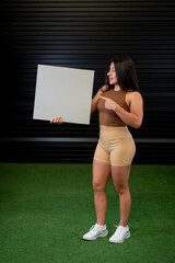 A standing female athlete holds a white board with her hands while pointing at it.