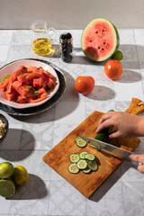 Hands of a woman delicately slicing fresh cucumber into thin rounds to prepare a vibrant Mediterranean salad featuring watermelon, feta cheese, and cucumber