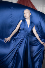 Obraz premium A bald model exhibits an elegant stance while draped in a voluminous blue dress, creating an artistic effect