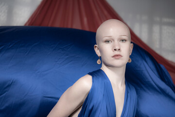 A bald model dressed in blue shows a contemplative gaze, set against a theatrical red and blue...
