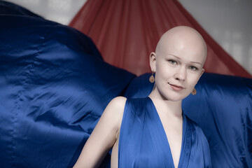 A bald model portrays a fierce elegance in a blue dress, with a subtle glance and dramatic blue...