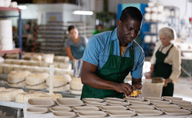African american man prepares pottery with a foam sponge - removes roughness and unevenness - obrazy, fototapety, plakaty