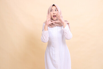 Fototapeta na wymiar young Asian Muslim woman standing to the candid camera with both hands near her mouth shouting making an announcement. Fashion, pointer, business and promotion concept