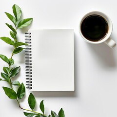 flat lay photograph showcasing blank white spiral notebook resting on table adorned with coffee cups and verdant green leaves, against minimalist white background.