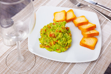 Fresh guacamole dip served with toasted bread on plate