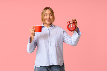 Happy adult woman with cup of coffee and alarm clock on pink background