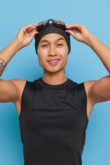 A man wearing a black tank top smiles with swim cap and goggles on