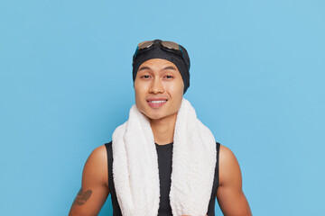 Man with a smile wearing swim cap and goggles with towel around his neck