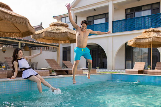 Happy young couple jumping into swimming pool