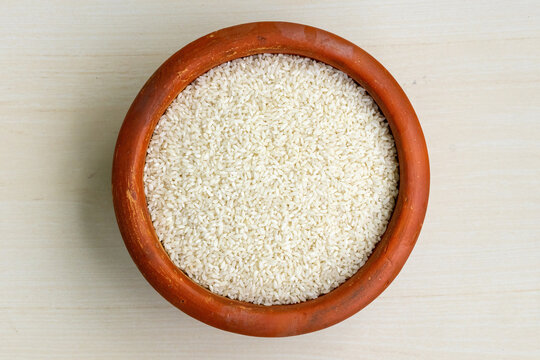 Food rice in an earthen pot on a wooden background. It is the Premium Chinigura Rice of Bangladesh which is used for cooking Polao, Khichuri, Biriyani, or the traditional Bangladeshi Payesh. Top view.