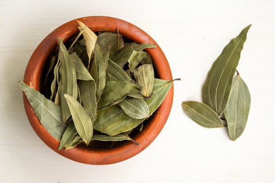 Dried bay leaves (Laurus nobilis) in an earthen pot on a wooden background. It is also known as Tej Pata, Cassia leaves, Cinnamomum tamala, Indian bay leaf, Indian bark, Malabar leaf, Bay laurel, etc.