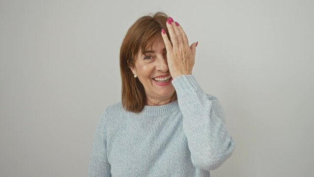 Confident, middle age woman with a fun, peeking gesture! covering one eye with hand, she's standing wearing a sweater, her smiling face radiates cheerfulness. isolated on a white background.