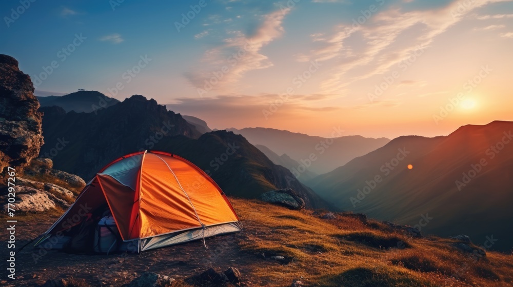 Poster a red tent is set up on a grassy hillside. the sun is setting in the distance, casting a warm glow o