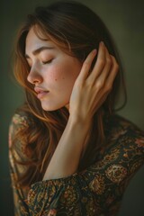 Fototapeta premium A woman with long brown hair and a floral print dress is looking at the camera. She has a hand on her ear and a hand on her shoulder. Concept of intimacy and vulnerability