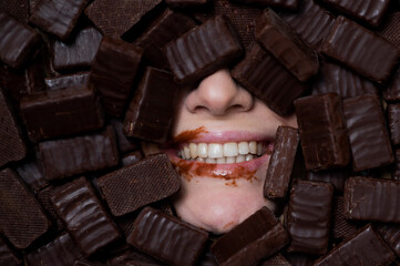 The face of a caucasian woman surrounded by sweets. The girl is smeared in chocolate. 
