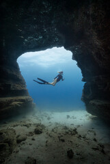 A female free diver poses in an underwater cave opening in the clear blue waters of Hawaii. Model release provided.