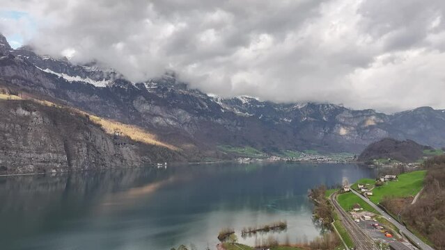 Drone clip showing a view over calm Walen lake surrounded by snowtopped mountains and lakeside village in the distance