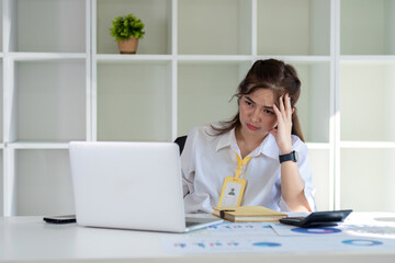 Asian businesswoman who is tired and has a headache from difficult work causing stress Sitting and looking at work at the desk in the office.