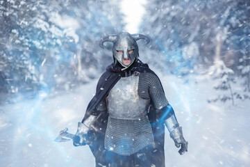 Portrait of a medieval fantasy warrior in a horned helmet, steel breastplate, chain mail with a two-handed ax in his hand, using a magic spell while standing against the backdrop of a winter forest. - obrazy, fototapety, plakaty