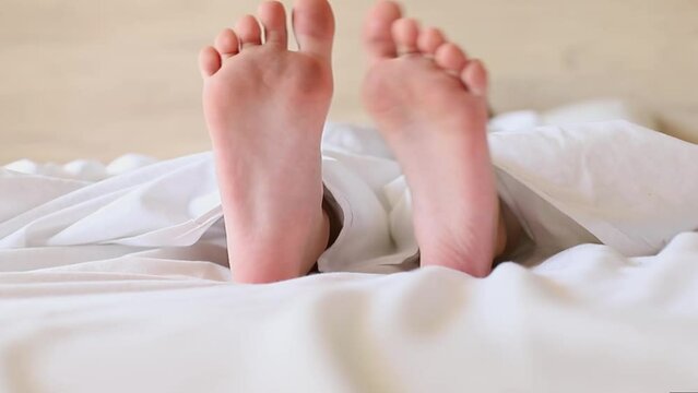 Little girl's feet stick out from under a white blanket at the morning. 