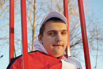 Young autistic guy on a walk in the park swinging on a swing