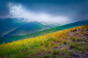 Thin ray of the sun breaks through thick rain clouds and illuminates the green hillside. Fabulous summer view of Svydovets mountain range in Carpathians, Ukraine. Beauty of nature concept background..