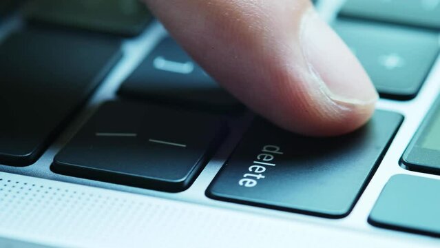 Finger of the computer user, he presses the delete button on the computer keyboard.	