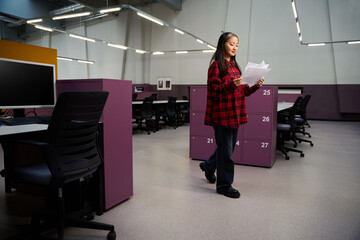 Young focused asian female IT employee going and reading documents