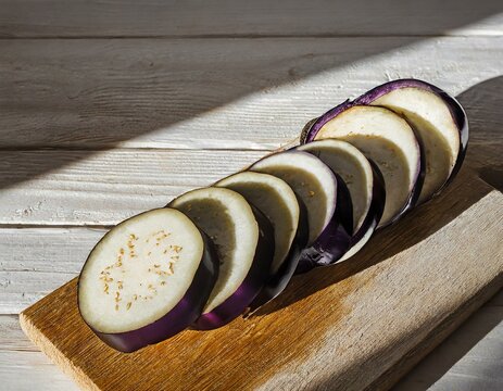 An eggplant sliced lengthwise, displaying the gradient from deep purple skin to cream-colored flesh, on a light wooden board.