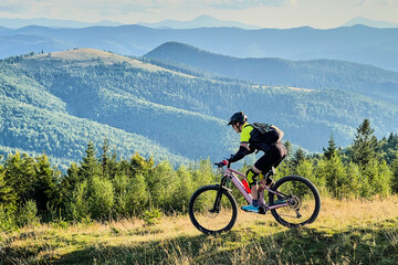 Cyclist man riding electric mountain bike outdoors. Male tourist biking along grassy trail in the...