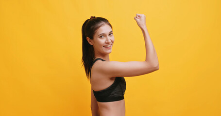 Young sportswoman shows physical strength. Isolated on yellow background in studio.